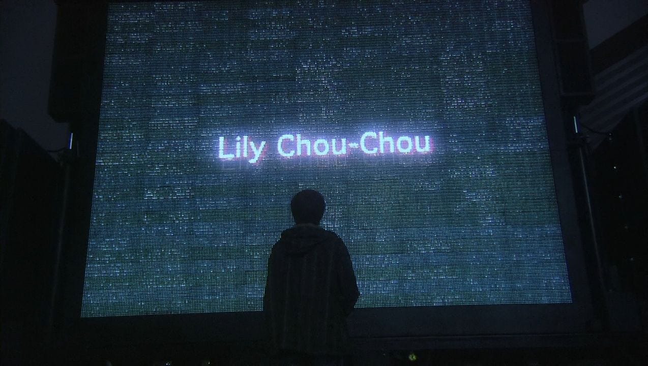 A figure facing the glowing Lily Chou-Chou concert screen