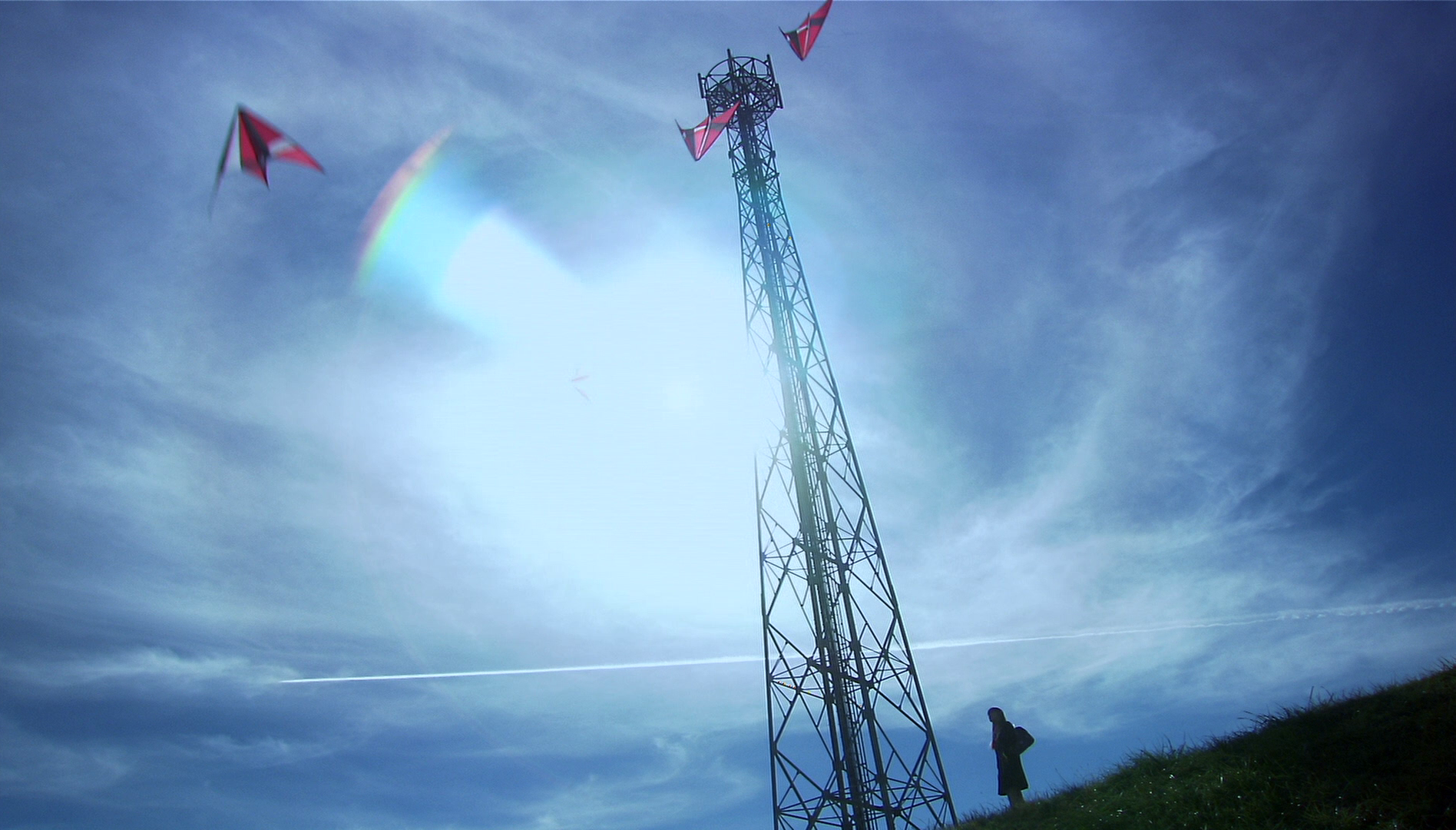 A transmission tower and red kites against a blue sky